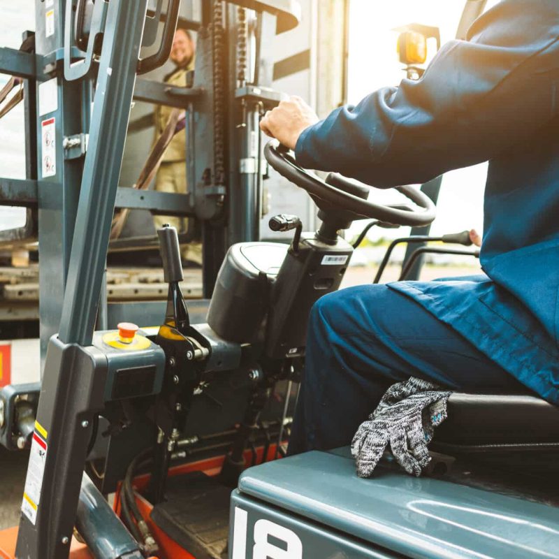 A Man On A Forklift Works In A Large Warehouse, Unloads Bags Of Raw Materials